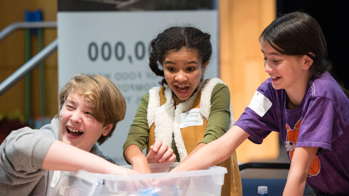 Three students reach their hands into a plastic bin.